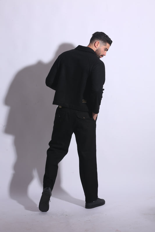 Person wearing a black coat and pants standing on a white floor with a shadow cast behind.