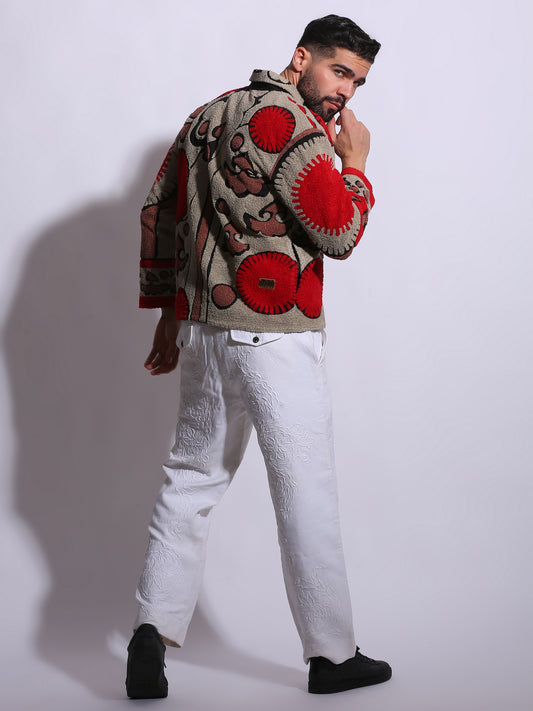 Man wearing a patterned sweater with red accents and white pants against a plain background