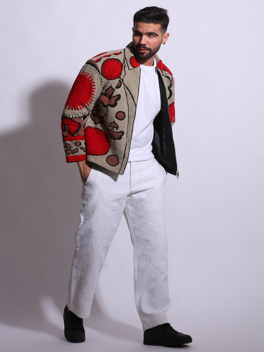 Man wearing a patterned jacket over a white shirt and pants on a plain background