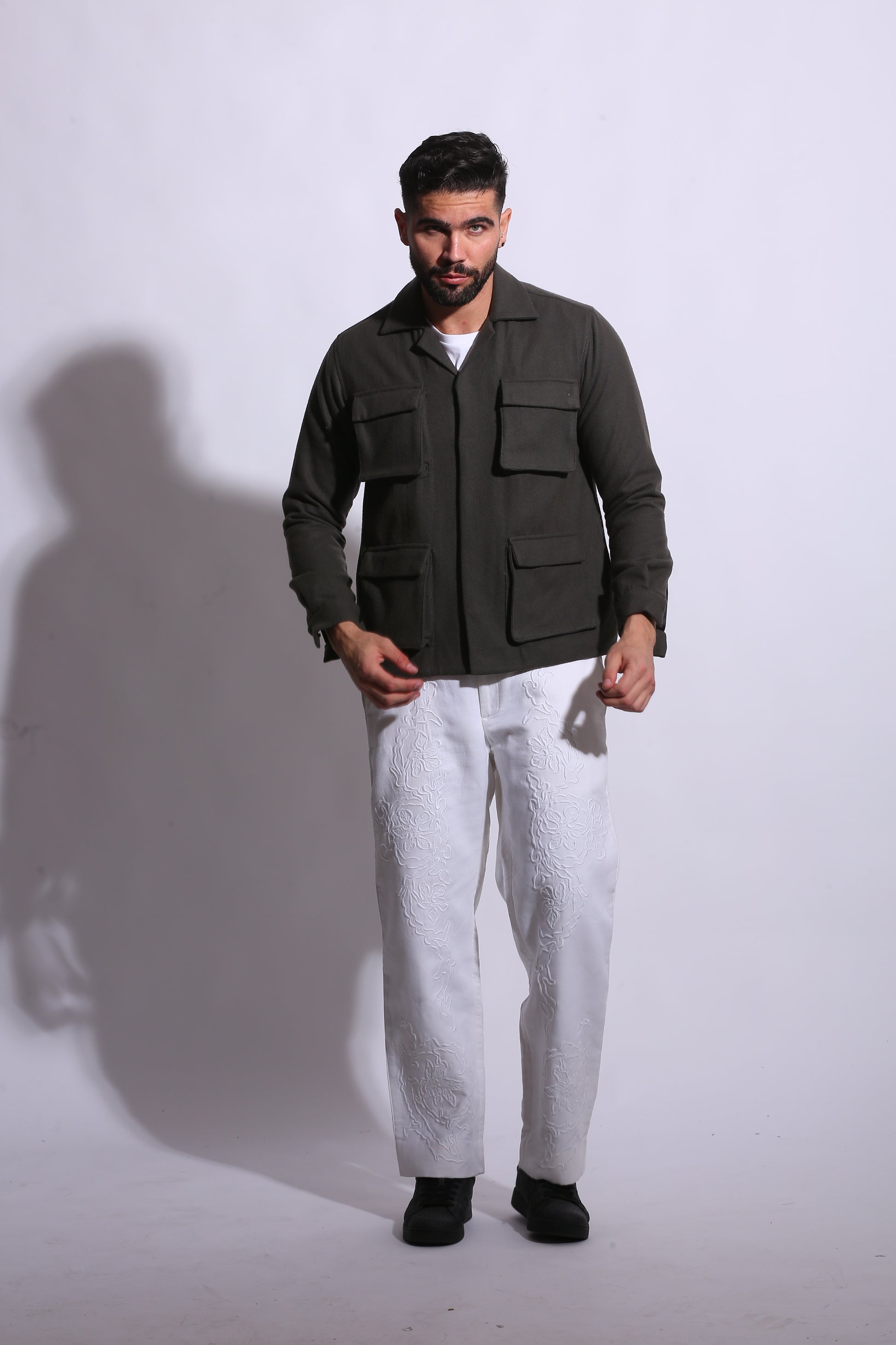 Man in a dark coat standing on a white floor with a plain background