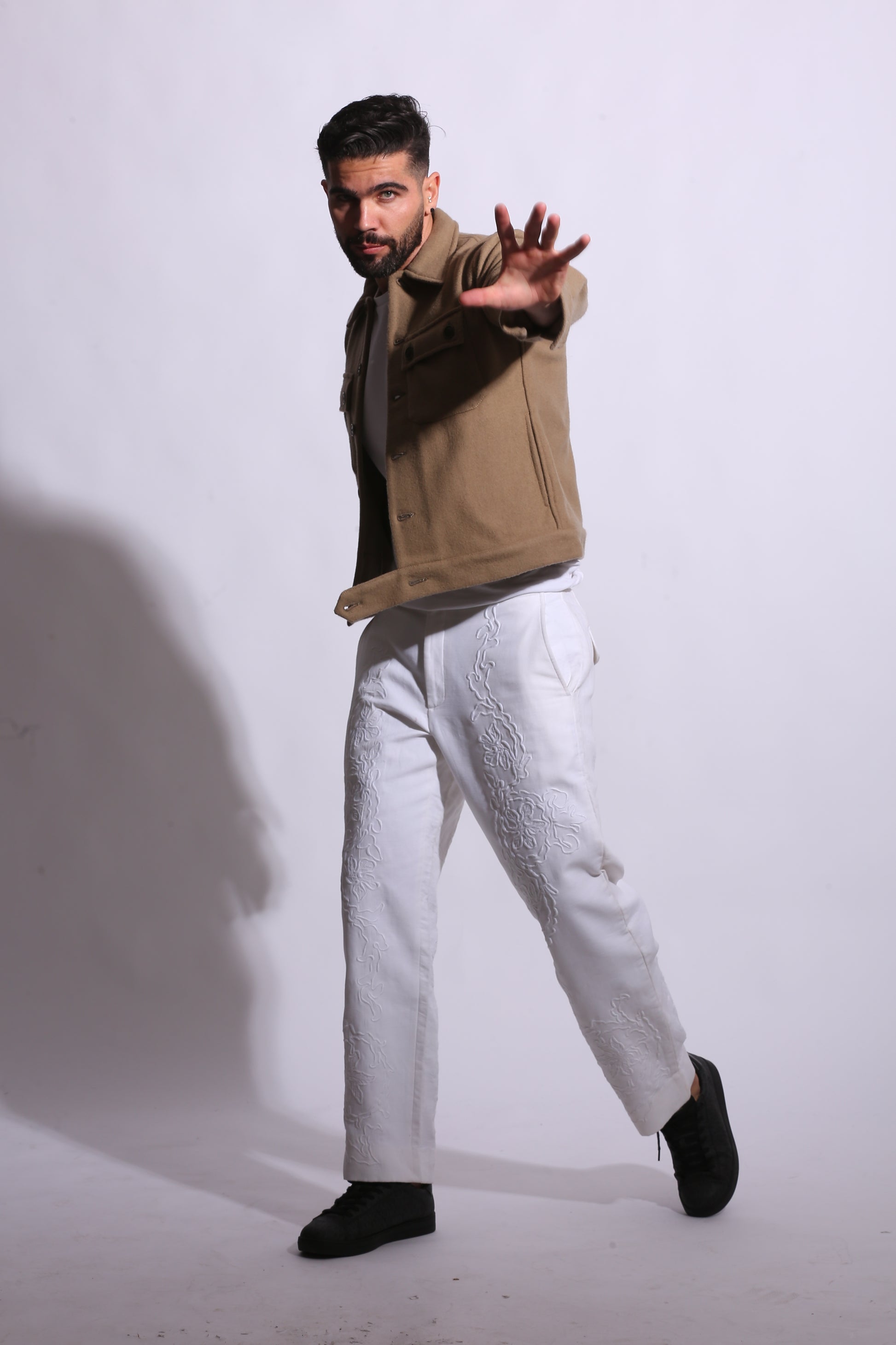 Person wearing a beige coat and white pants on a white background