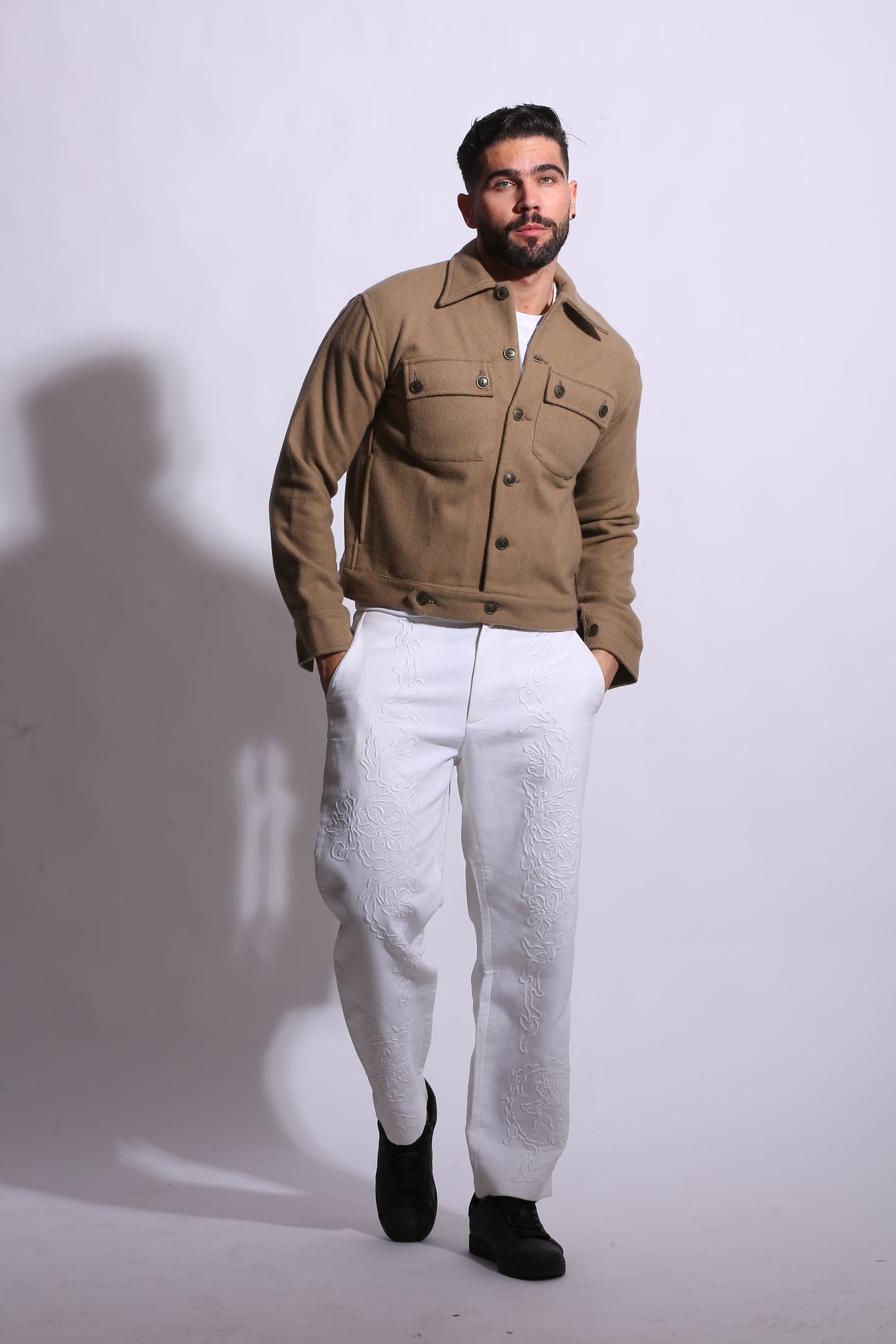 Man wearing a brown coat and white pants on a plain background