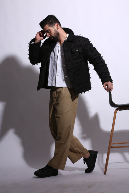 Man in a black coat and beige pants standing on a white background