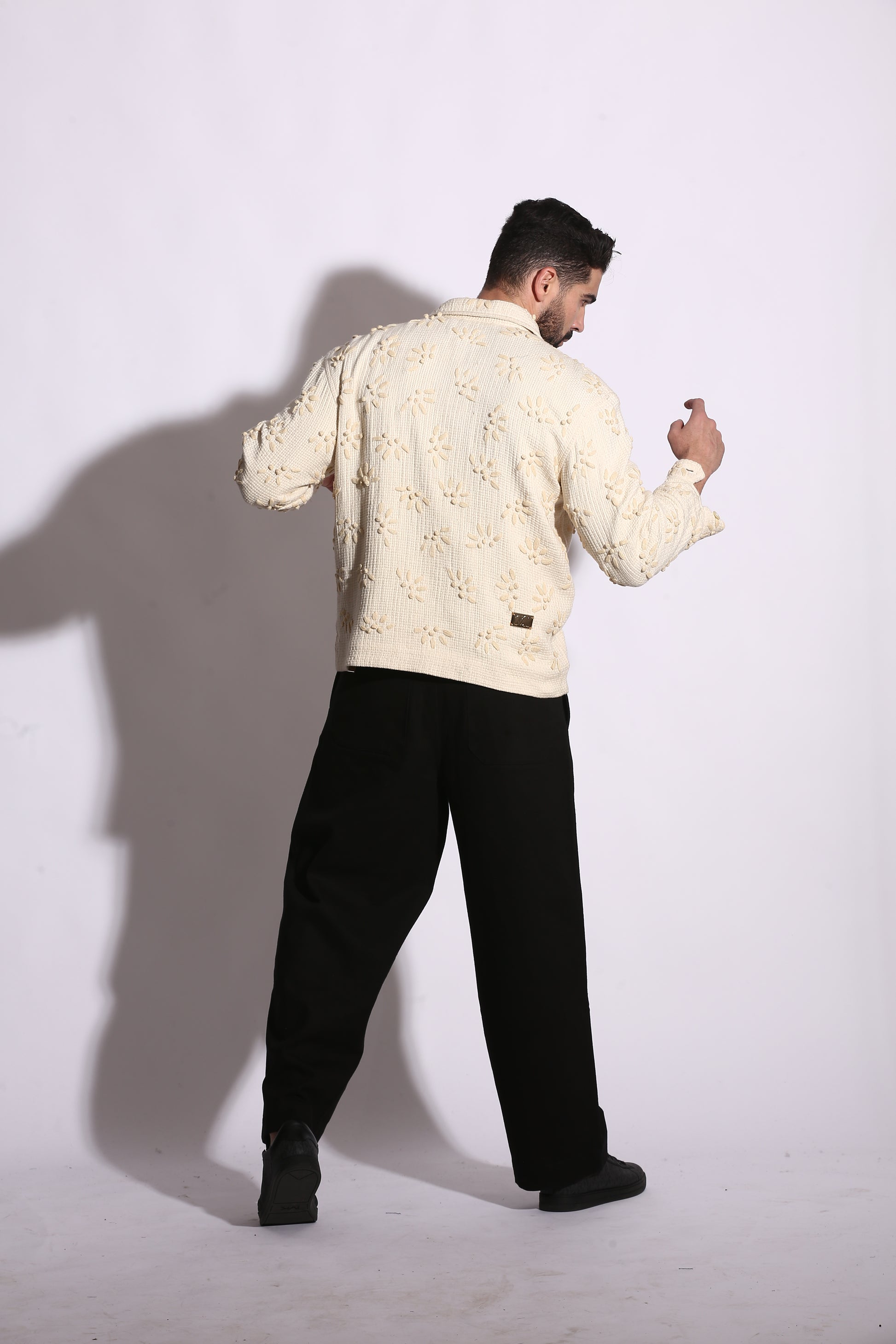 Person wearing a beige patterned shirt and black pants on a white background